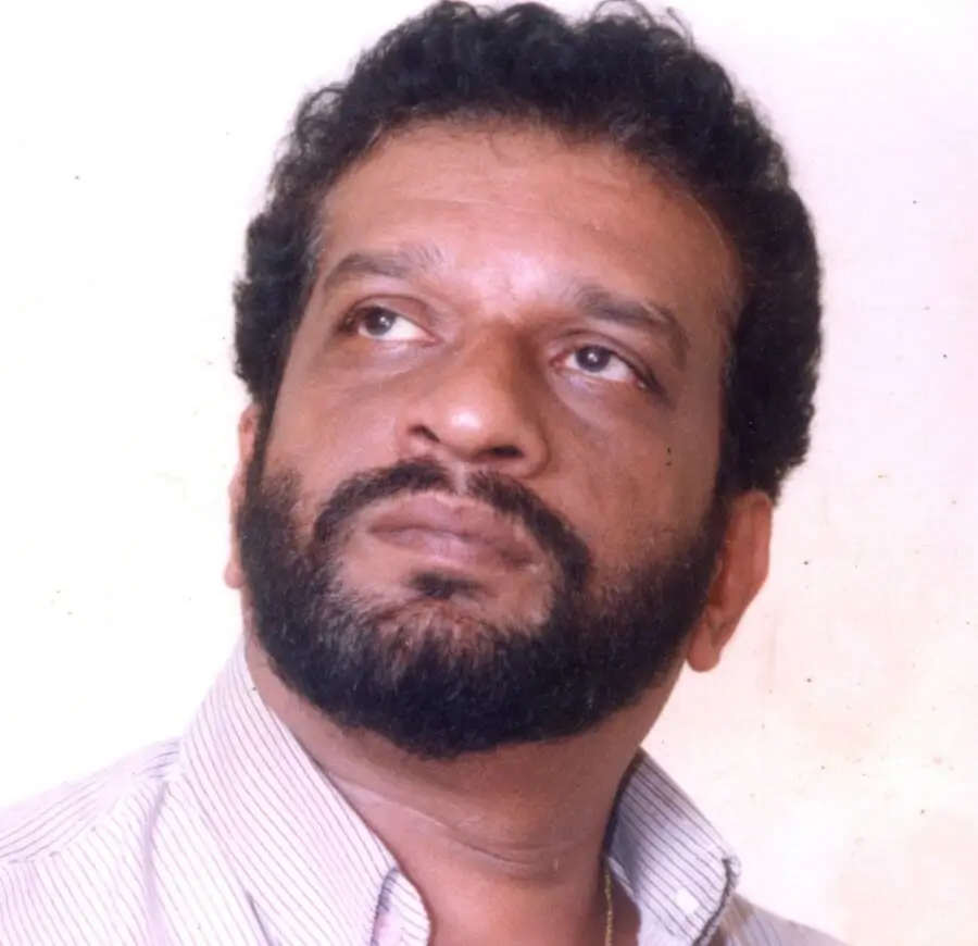 A bearded man dressed in a shirt, showcasing a calm demeanor and poised stance.
