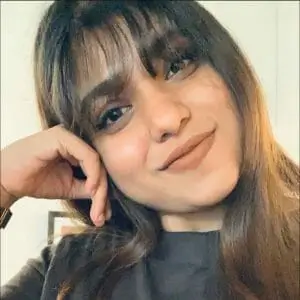 A woman with long hair wearing a black shirt, standing confidently against a neutral background.