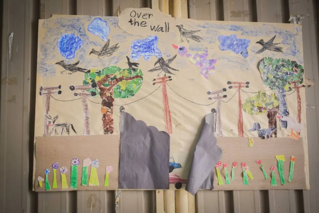 A child's drawing depicting a colorful bird perched on a tree in a vibrant green field under a clear blue sky.