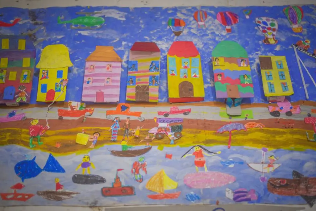 A vibrant beach scene painting featuring boats and people enjoying the sun and surf.