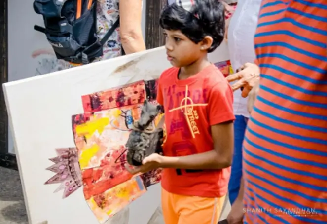 A young girl proudly holds a piece of art displayed in a gallery setting, showcasing his creativity and enthusiasm.