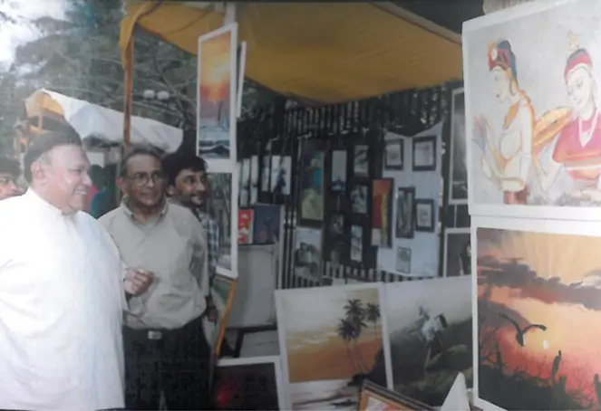 Two men are positioned next to each other, one displaying a painting while the other observes with interest.