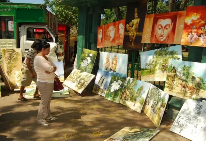 A woman examines various paintings displayed at an outdoor market, showcasing her interest in art and creativity.