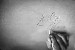 An individual engaged in drawing a figure on paper, showcasing their artistic skills and concentration.