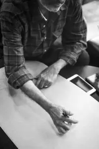 A man at a table, intently examining a drawing placed on its surface.