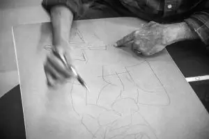A man focused on sketching on a piece of paper, showcasing his artistic talent and concentration.