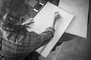 An older gentleman diligently drawing on paper with a pencil, capturing his creativity and concentration.
