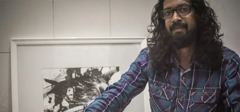 A man with long hair stands before a black and whitel painting, contemplating the artwork with a thoughtful expression.