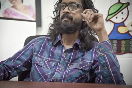 A man with long hair is seated at a desk, focused on his work in a well-lit environment.