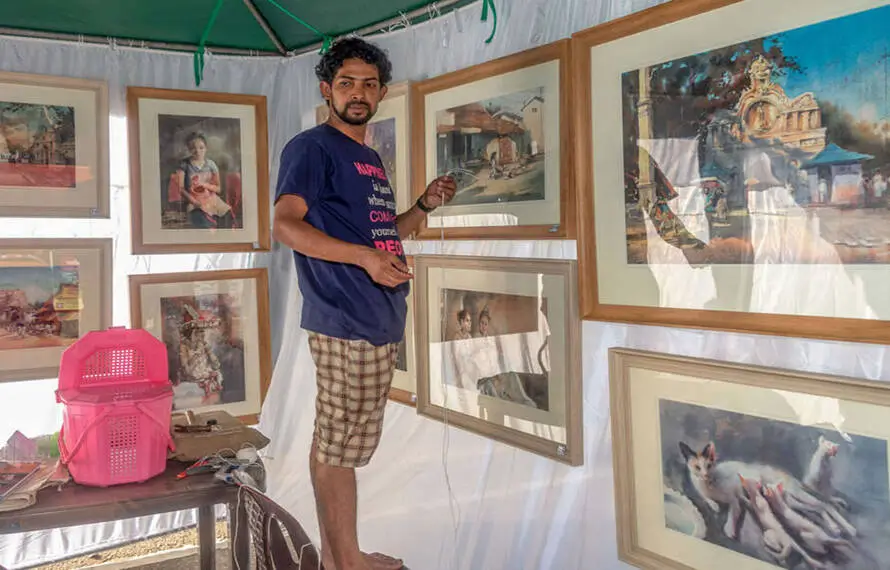 A man is positioned in front of a tent adorned with pictures, seemingly engaged in the act of hanging more images.