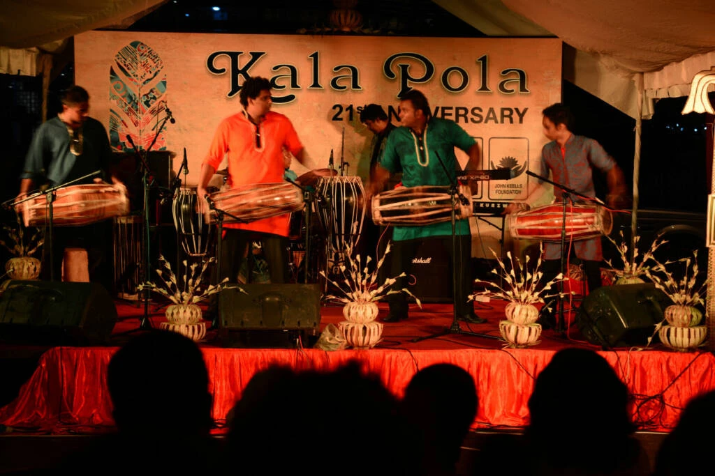 A diverse group of musicians energetically playing drums together on stage, creating a vibrant atmosphere