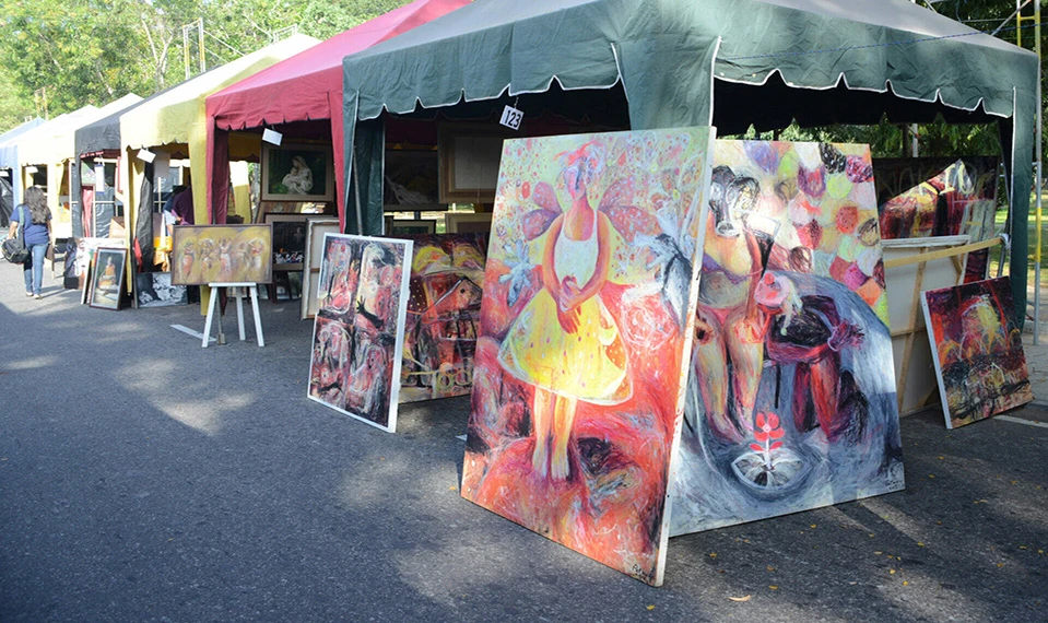 Tents with a white canopy displays various paintings in front, creating a vibrant outdoor art showcase.