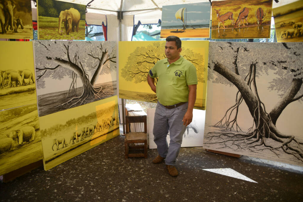 A man stands before a large display of various paintings, admiring the artwork on the walls around him.