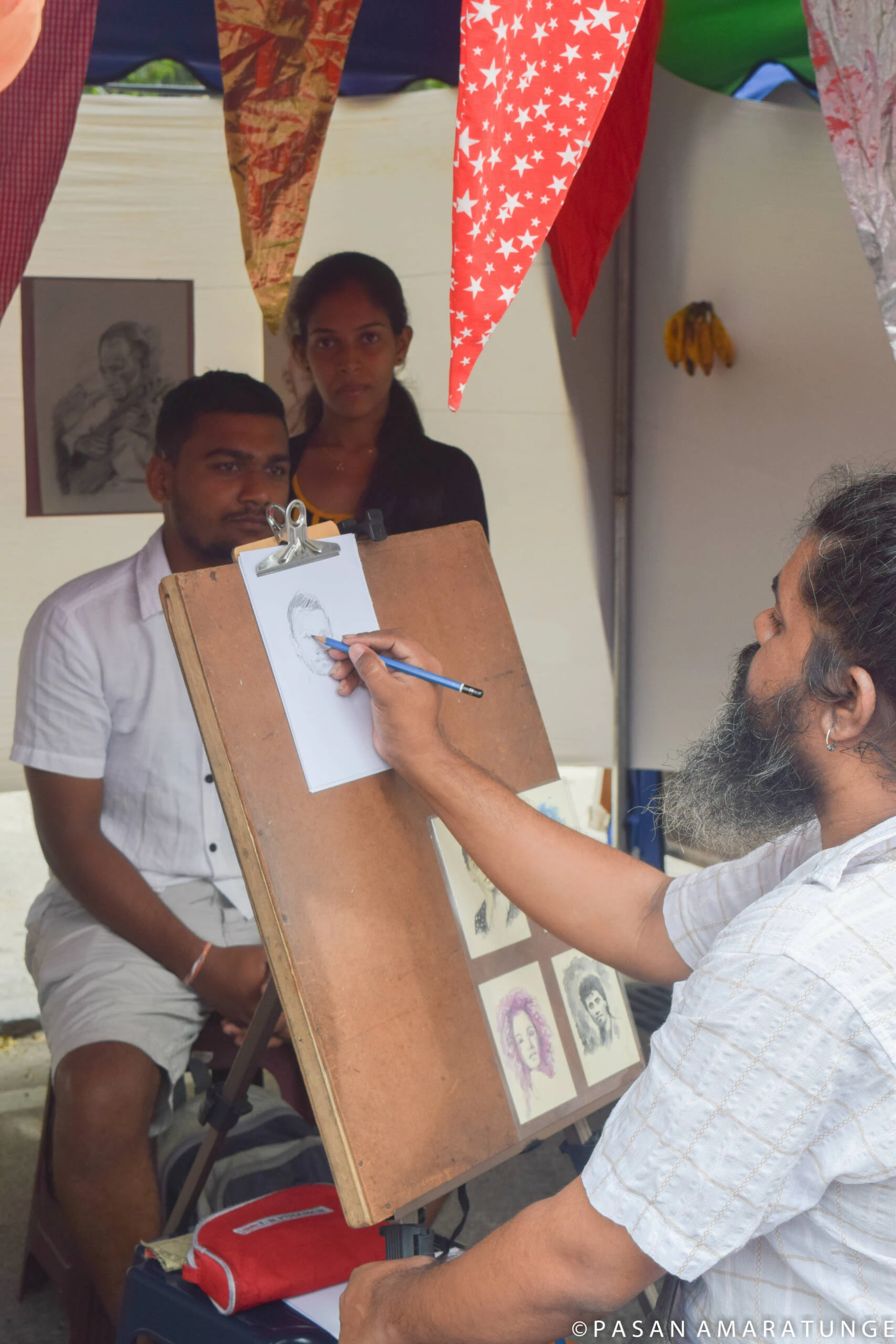 At an outdoor event, a man is focused on drawing on paper, capturing the essence of the lively surroundings.