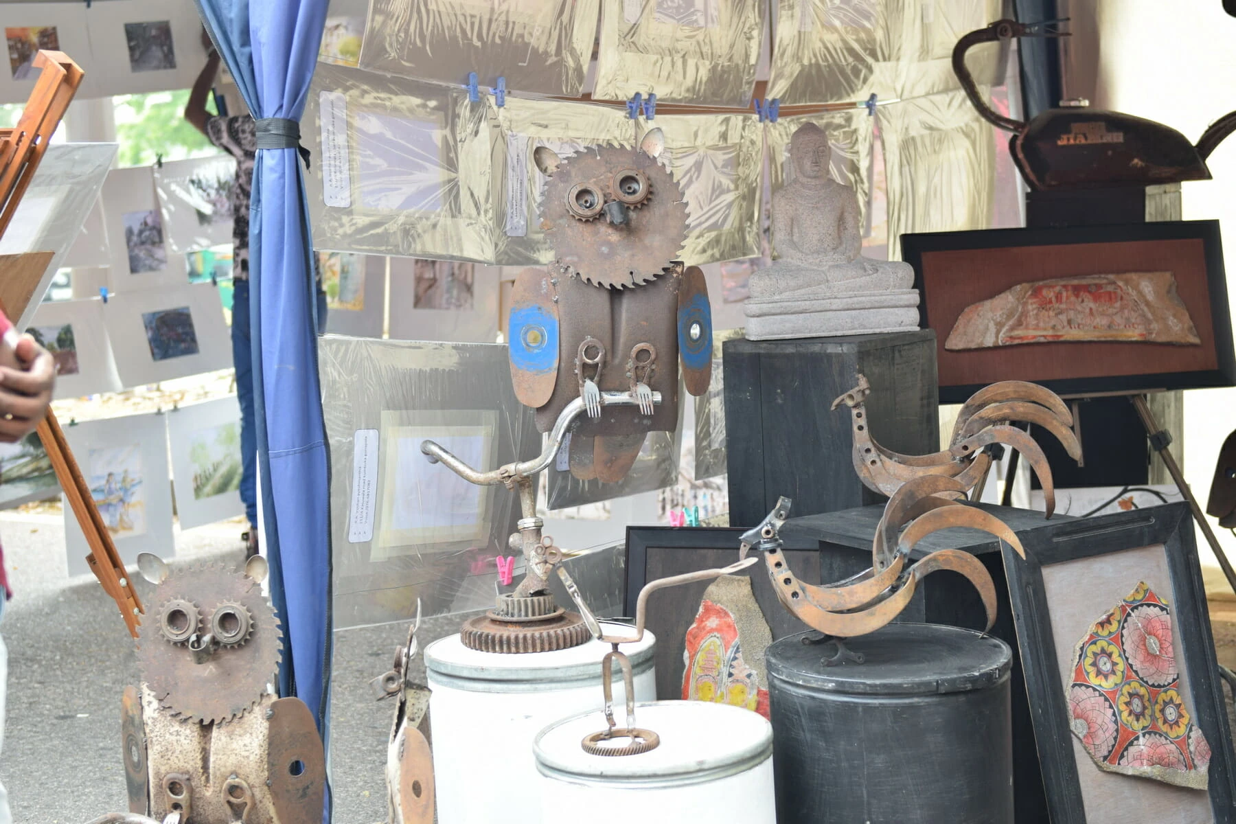 A man stands in a tent, holding a wooden stick, surrounded by various wooden art pieces.