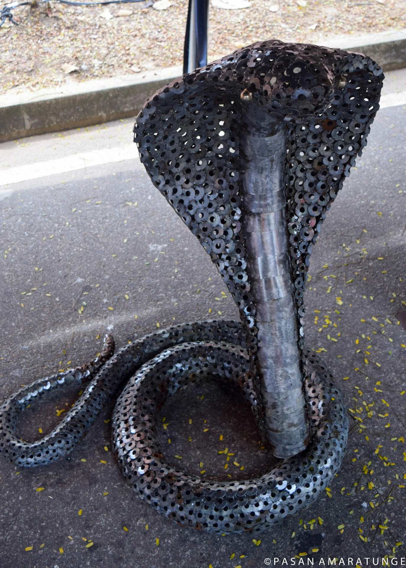 A cobra sculpture crafted from metal chains, resembling wooden art, displayed in a tent setting.