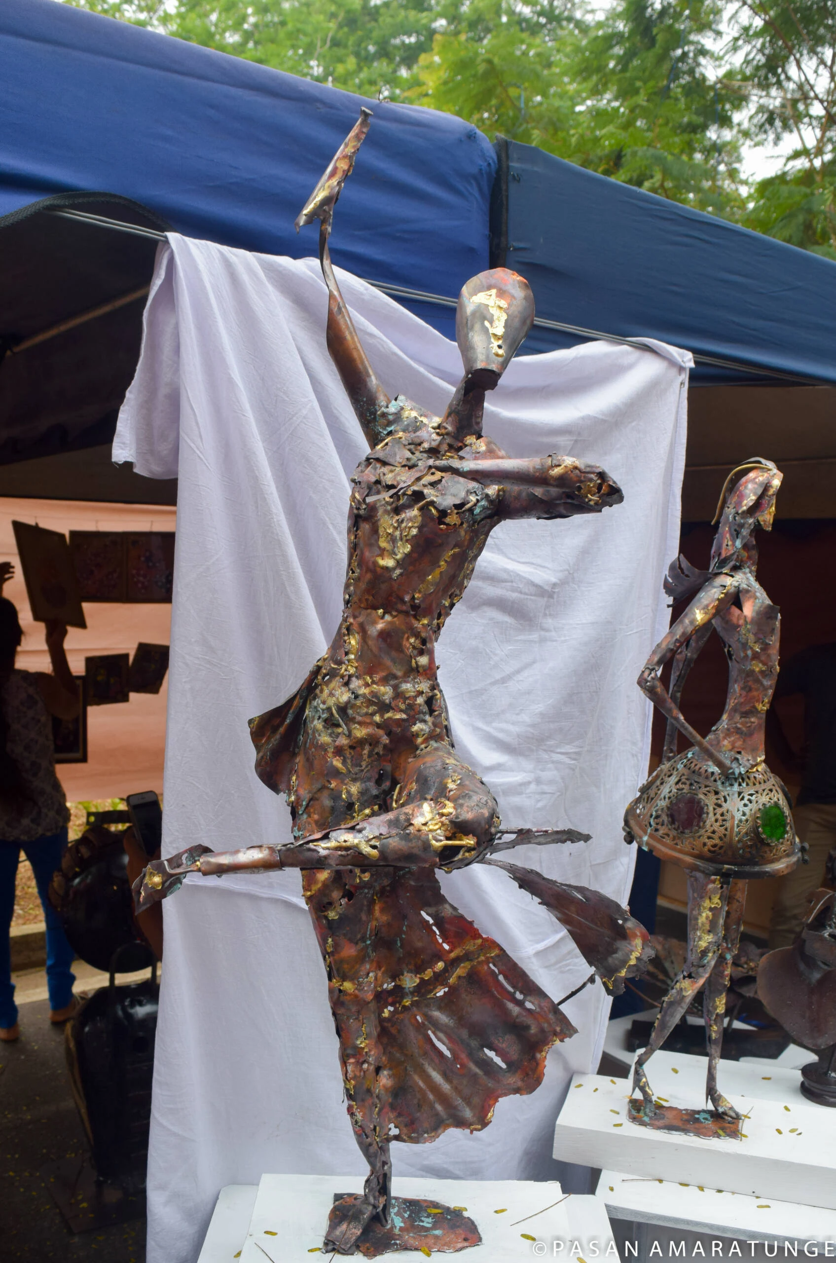 A metal statue of a woman holding a sword, displayed in a tent, showcasing intricate craftsmanship and artistry.