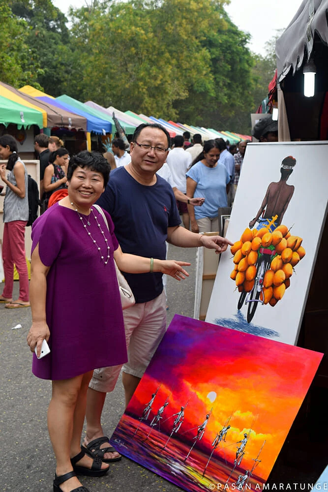 A man and woman stand beside a painting, engaged in conversation and appreciating the artwork together.