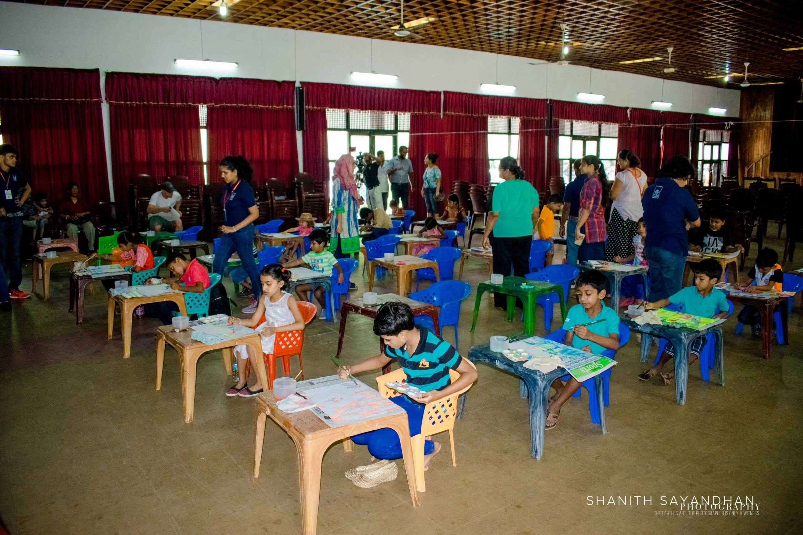 A classroom scene with children at desks, focused on painting, with books and papers scattered around.
