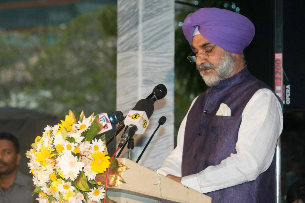 A indian man wearing a purple turban delivers a speech at a podium, engaging the audience with his presentation.