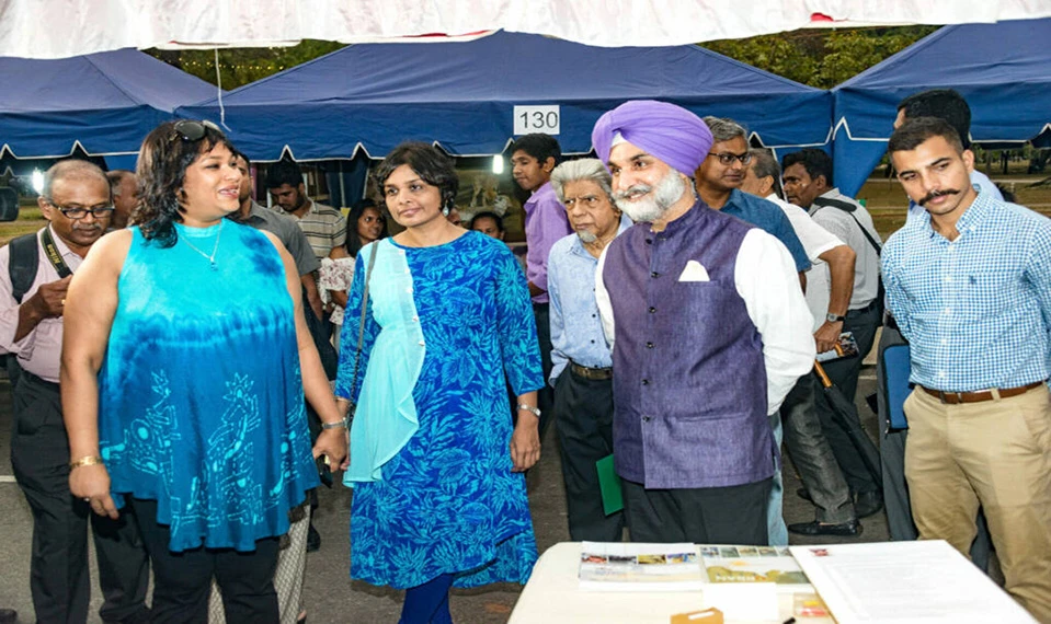 A diverse group of individuals gathered around a table, with a man in a turban at the center of the discussion.