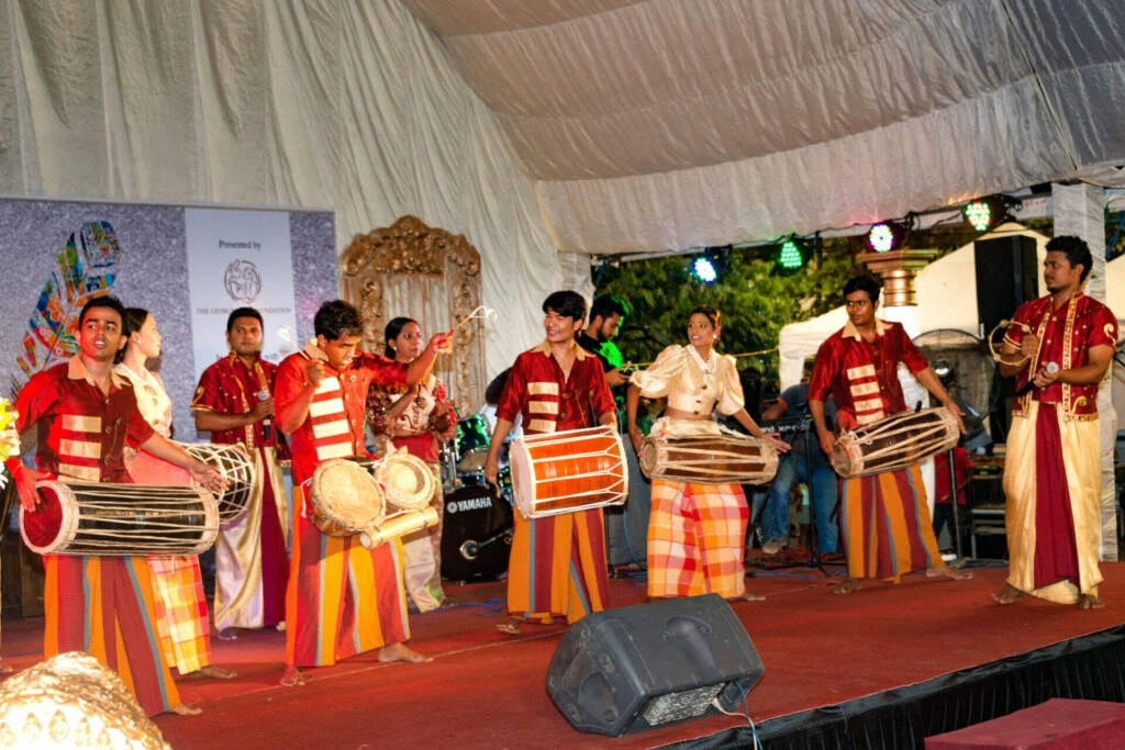 A diverse group of individuals in traditional attire performing energetically on stage, showcasing cultural heritage and artistry.