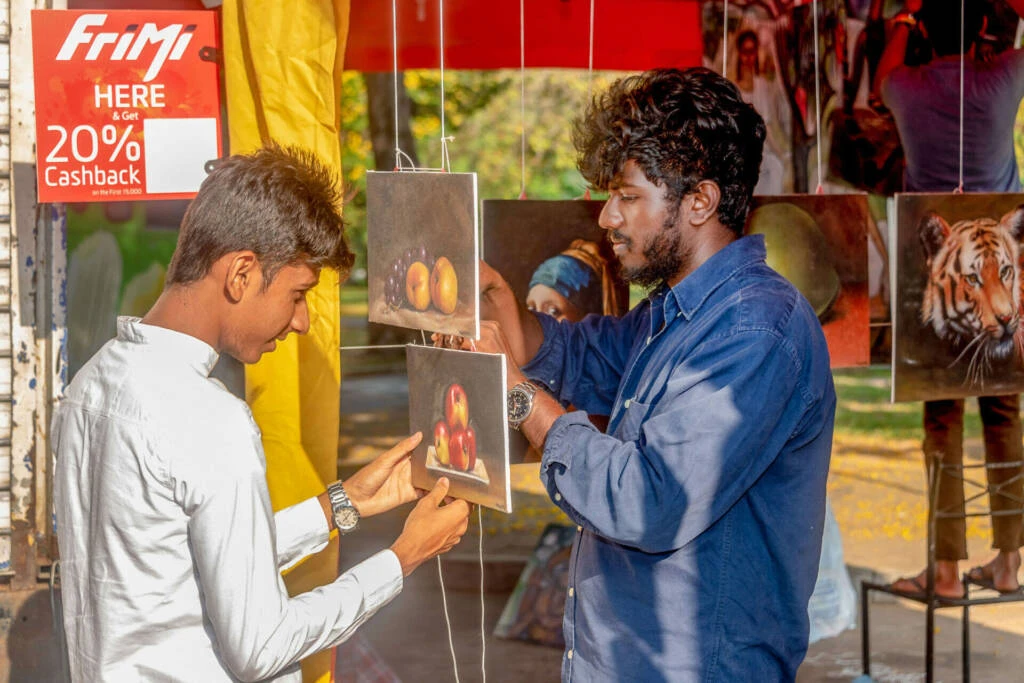 Two individuals stand beside a table displaying various pictures and books, engaged in conversation or observation.