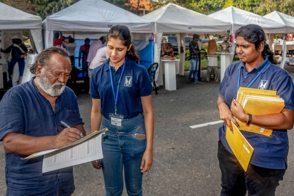 A group of individuals walking along a street lined with blue tents, creating a vibrant outdoor atmosphere.