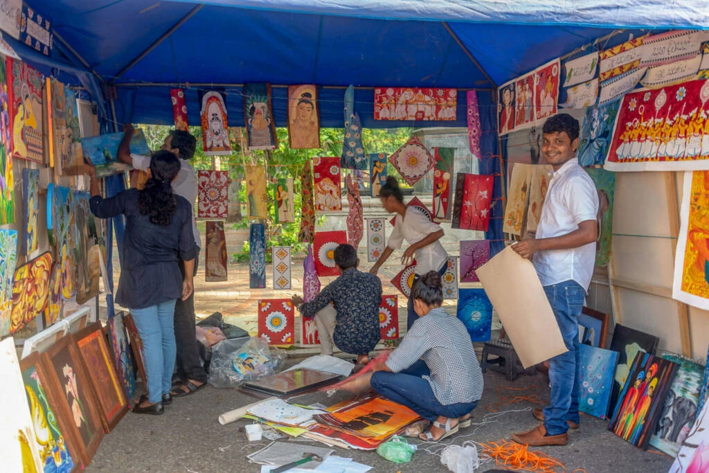 A man and woman stand side by side, engaged in conversation at an art show, surrounded by various artworks.