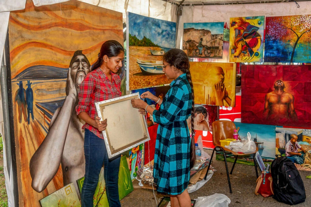 Two men engaged in conversation beneath a tent adorned with various sculptures.