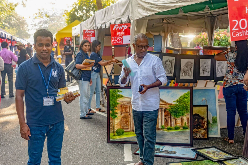 A man seated on a bench beside an artistic sculpture in a serene outdoor setting.