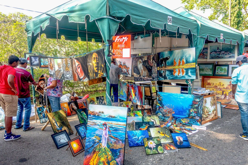 A man and woman admire colorful paintings at an outdoor market, surrounded by vibrant art displays and a lively atmosphere