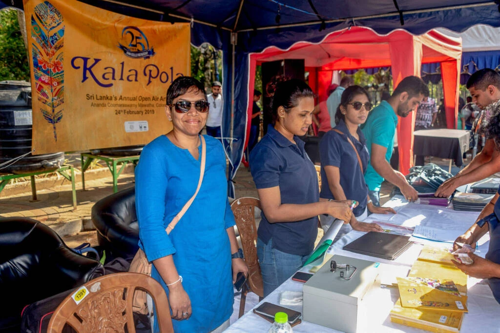 Men and monk standing side by side, engaged in conversation at an art show, surrounded by various artworks on display.