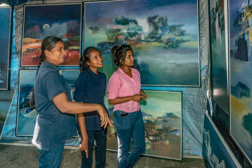 A man stands on a chair, hanging paintings on a tent adorned with various pictures.