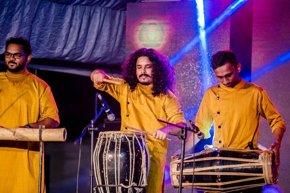 Three men energetically playing drums on stage, showcasing their musical talent and cultural heritage.