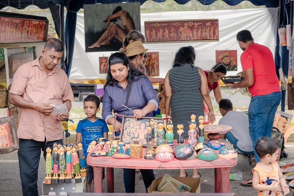 A man seated on a chair paints a child's face, creating a joyful and artistic moment between them.