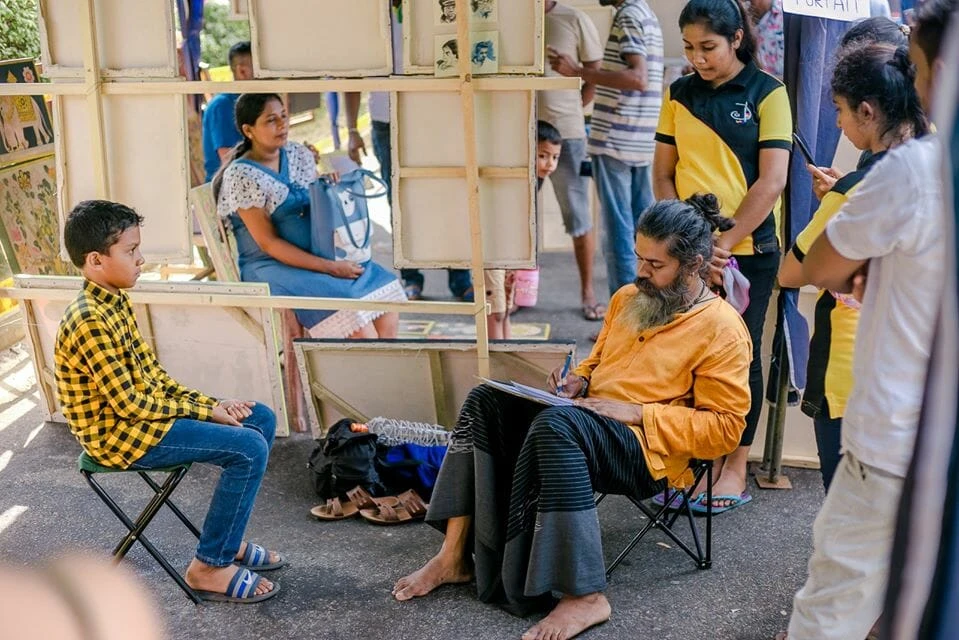 A man converses with another man at an outdoor market, surrounded by various stalls and shoppers.