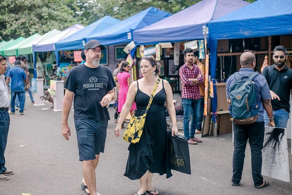 Two men engaged in conversation beneath a tent adorned with various paintings on the walls.