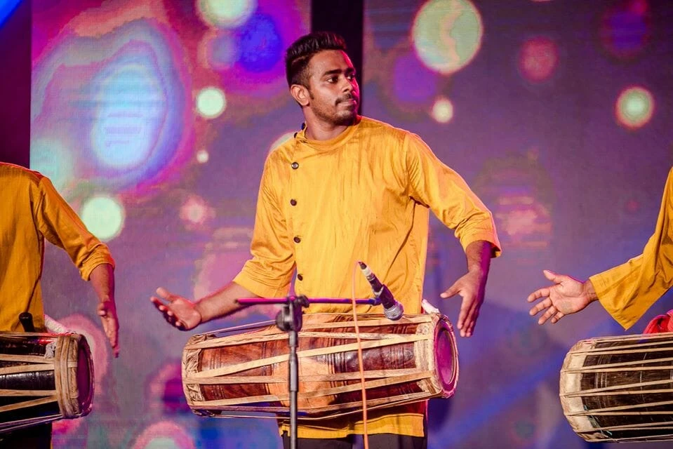 Three men gather around a table displaying various paintings, engaged in discussion and observation.