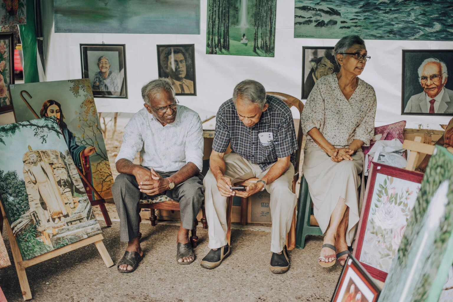 Three senior people sitting on chairs, engaged in looking at pictures, sharing memories in a cozy atmosphere.