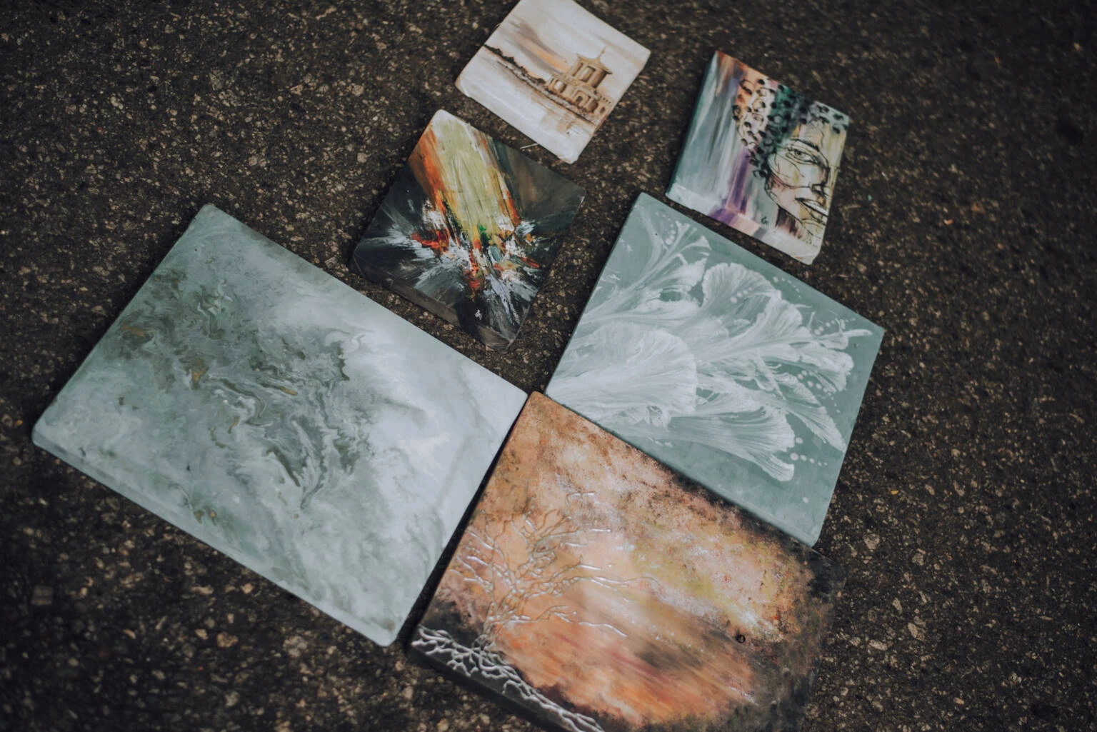 A collection of six paintings displayed on the ground, showcasing various artistic styles and vibrant colors.