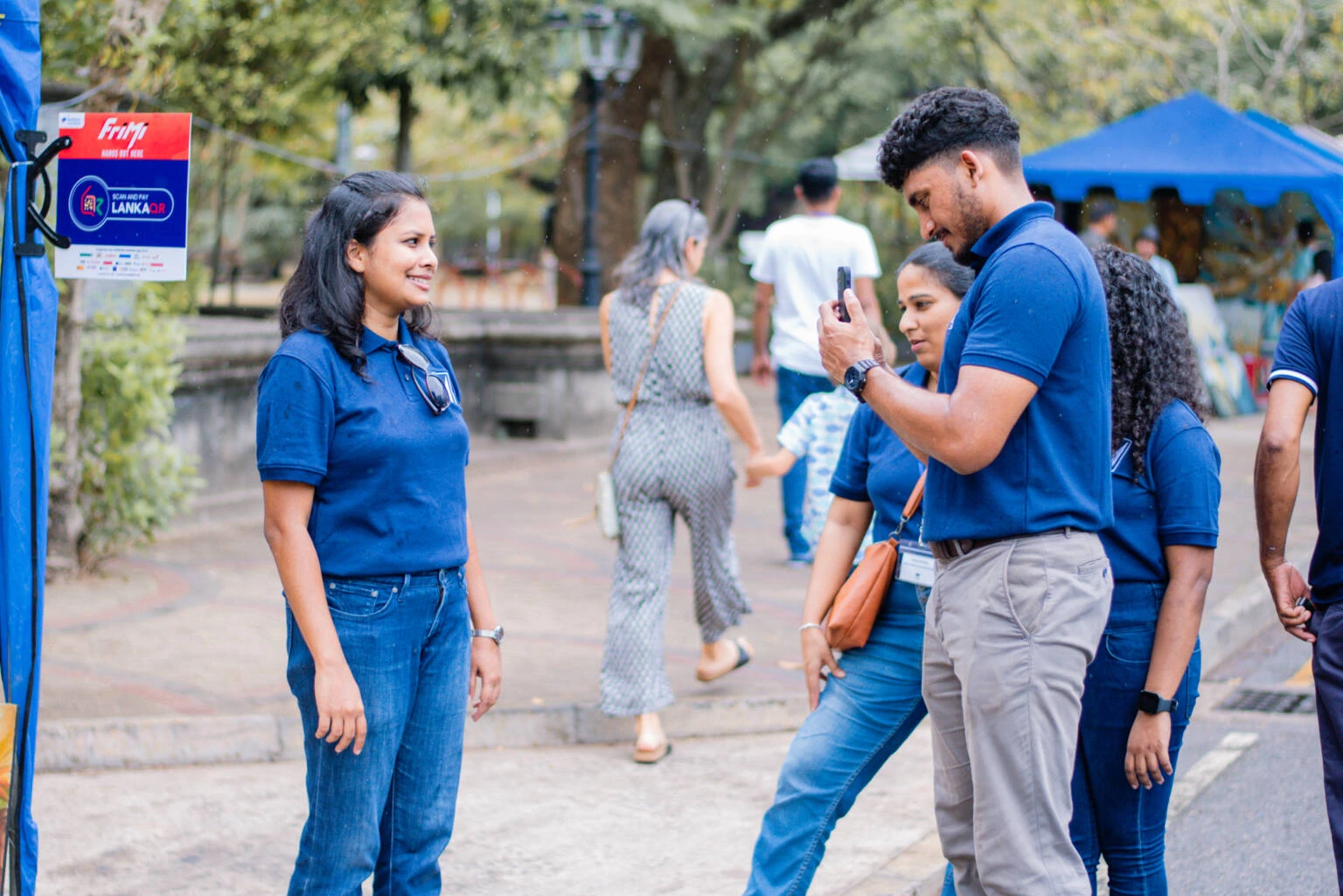 Several people of various backgrounds standing together near a blue tent, enjoying a social gathering in a natural environment.