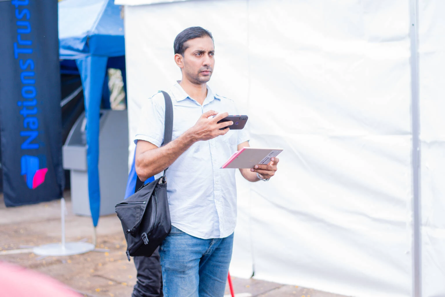 A man holds a black bag in one hand while his other hand is occupied with a phone.