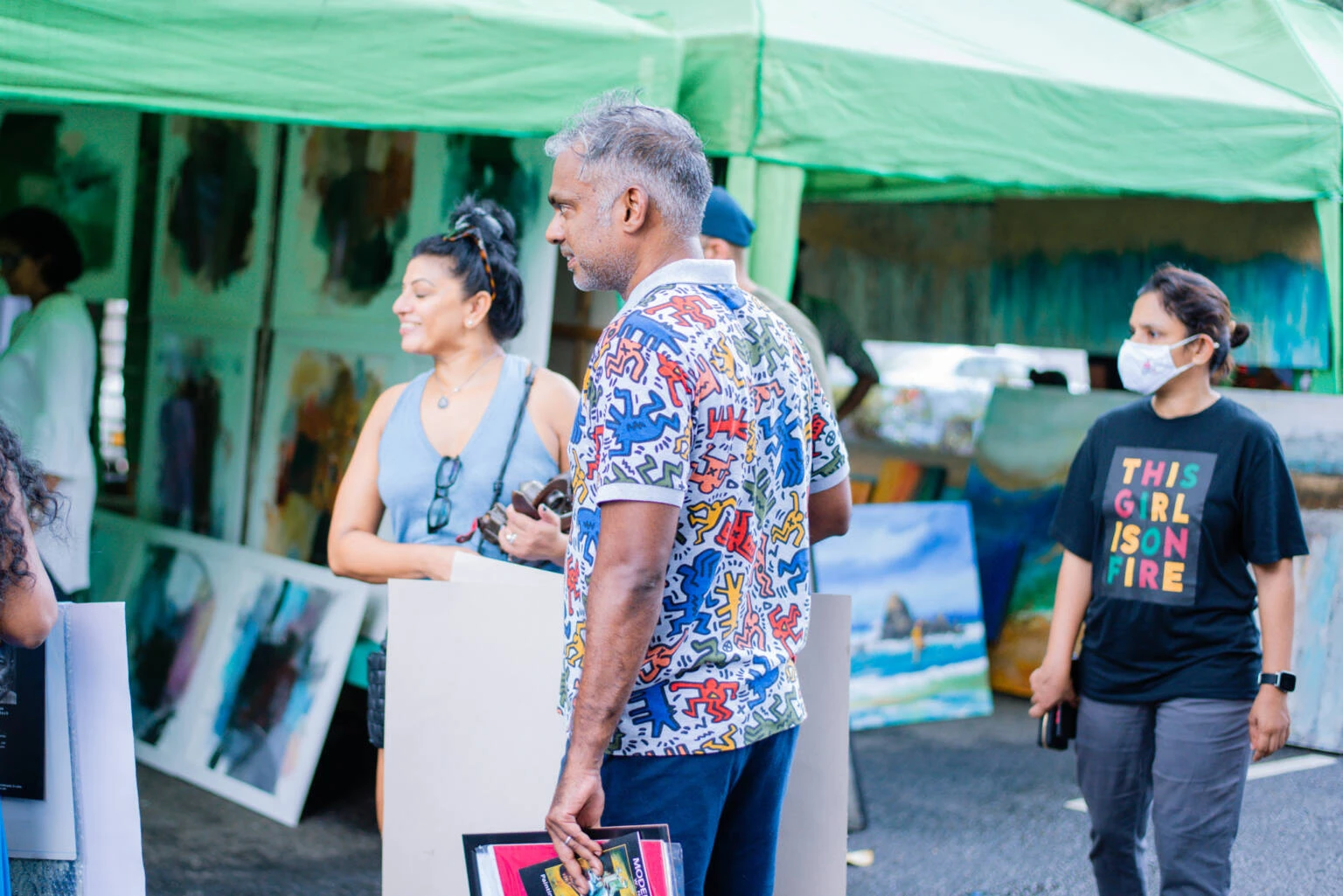 A diverse group of people gathers at an outdoor art fair, engaging with various art displays and enjoying the vibrant atmosphere.