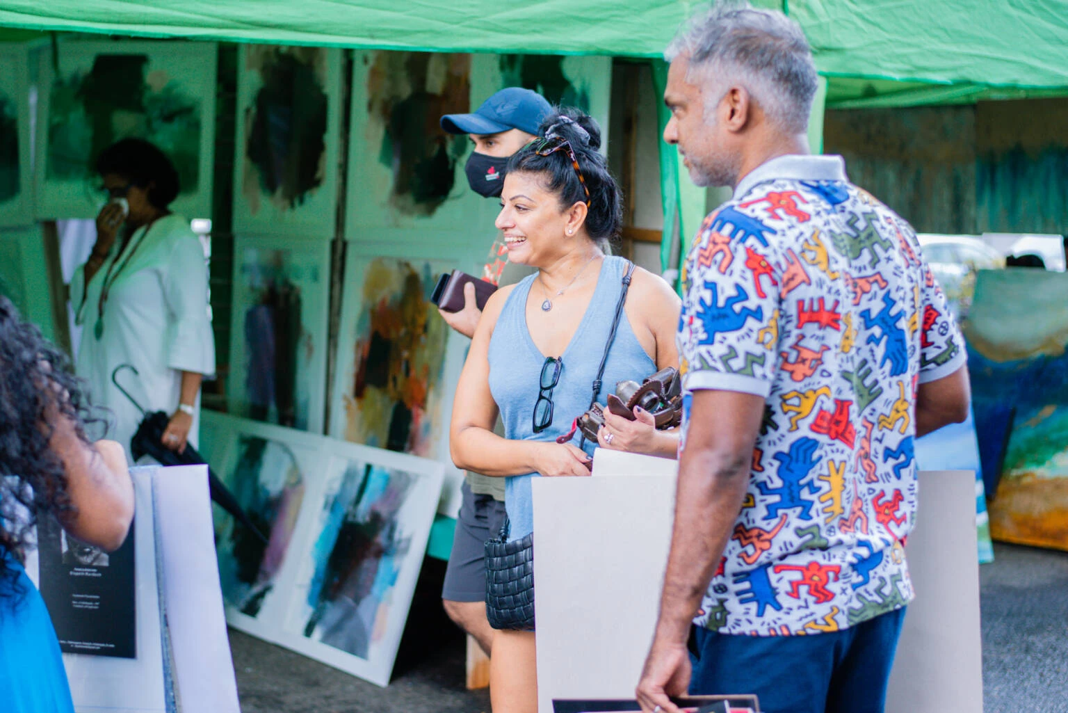 Attendees explore an outdoor art fair, surrounded by colorful artworks and engaging in conversations amidst a lively setting.