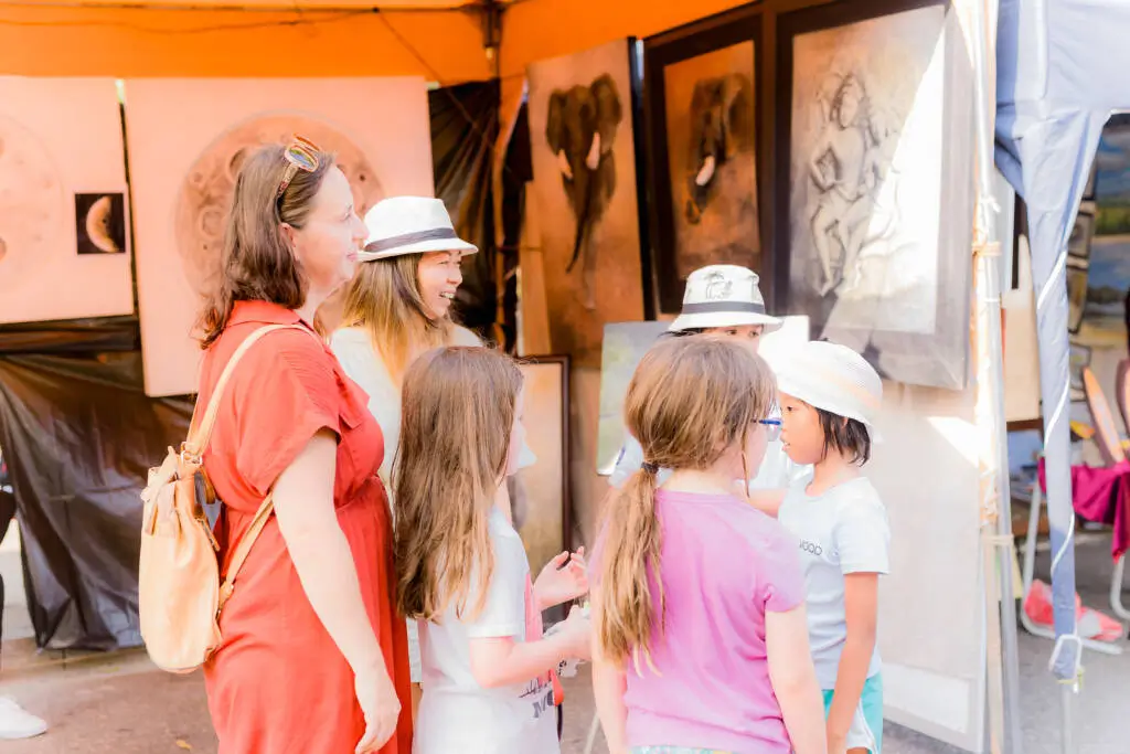 A diverse group of individuals gathered around a tent adorned with various colorful paintings.
