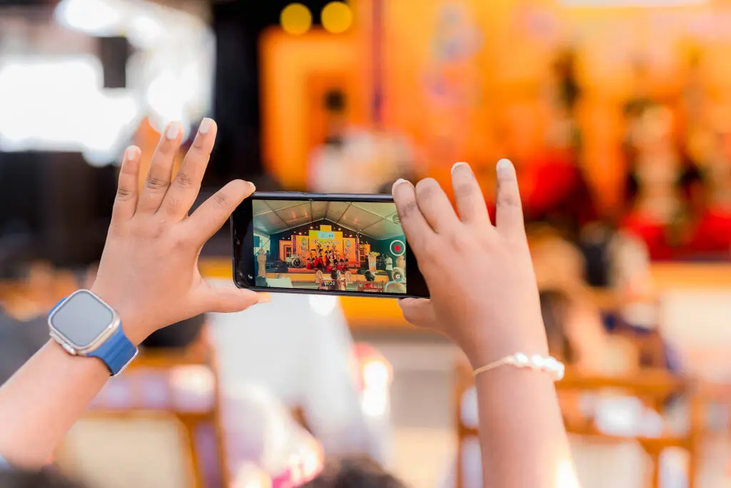 A person captures a photograph of a stage performance using a camera, focusing intently on the scene before them.