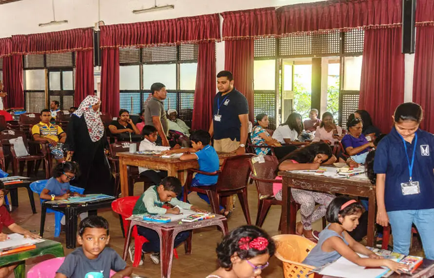 Children engaged at desks in a classroom, surrounded by drawing papers, focused on their learning activities.